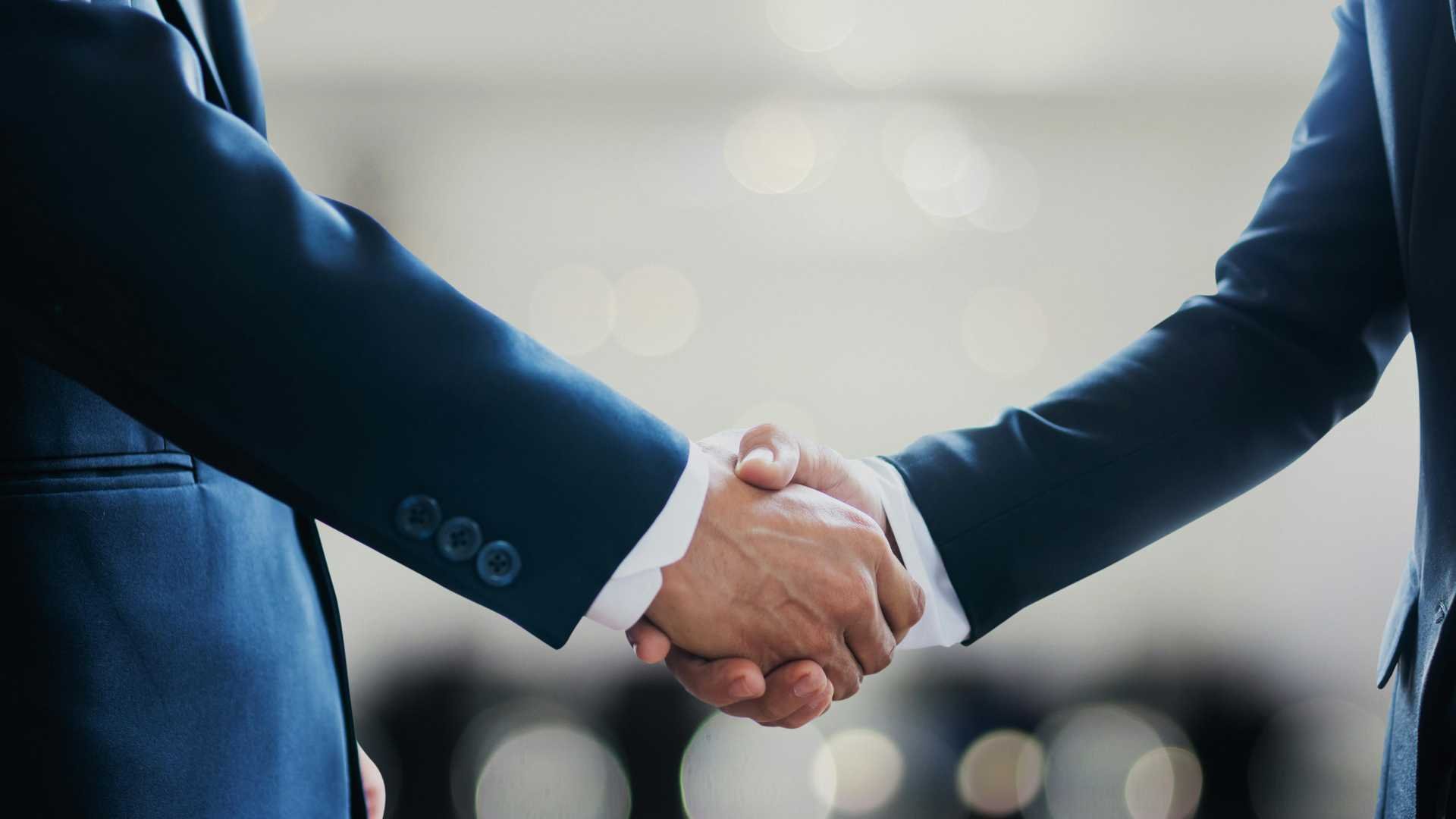 Two business people shake hands. They are wearing blue suits.