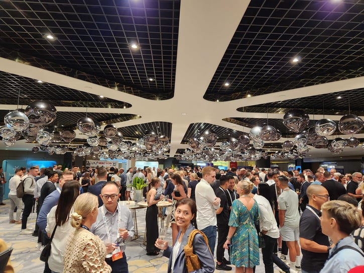 A crowded indoor event space filled with people networking, illuminated by large decorative hanging lights.
