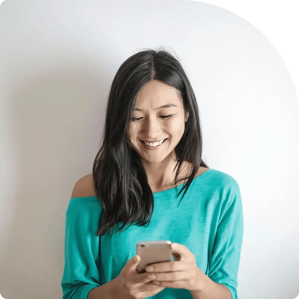 A smiling woman in a teal shirt looks at her phone.