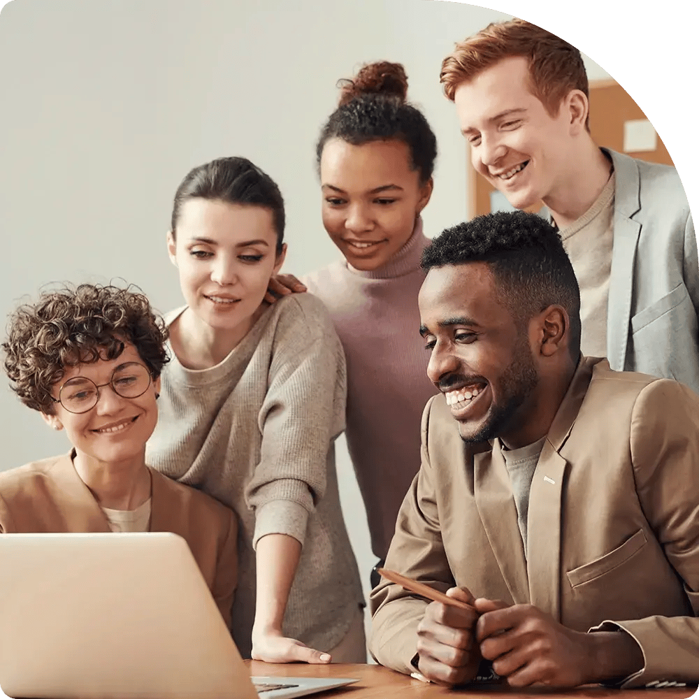 A diverse group of five people happily gather around a laptop, smiling and engaged. They appear to be collaborating or enjoying a successful project.