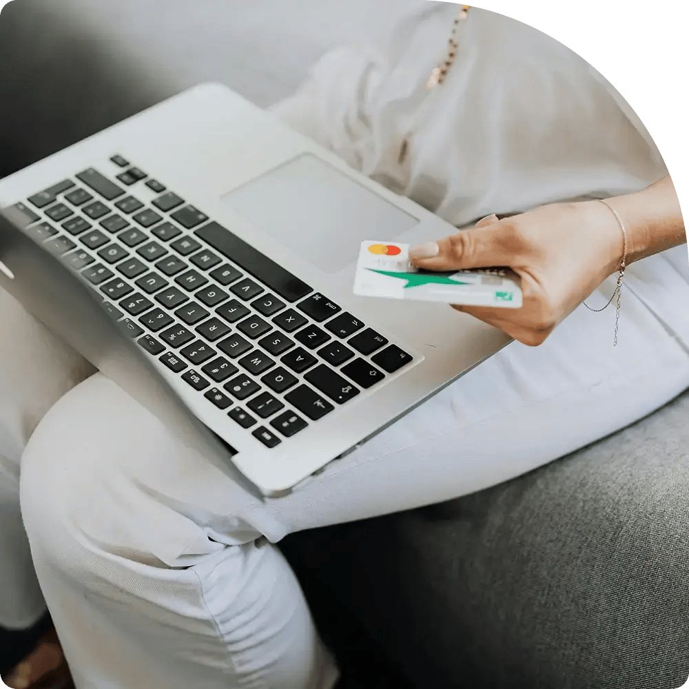 Person seated with a laptop on their lap, holding a credit card.