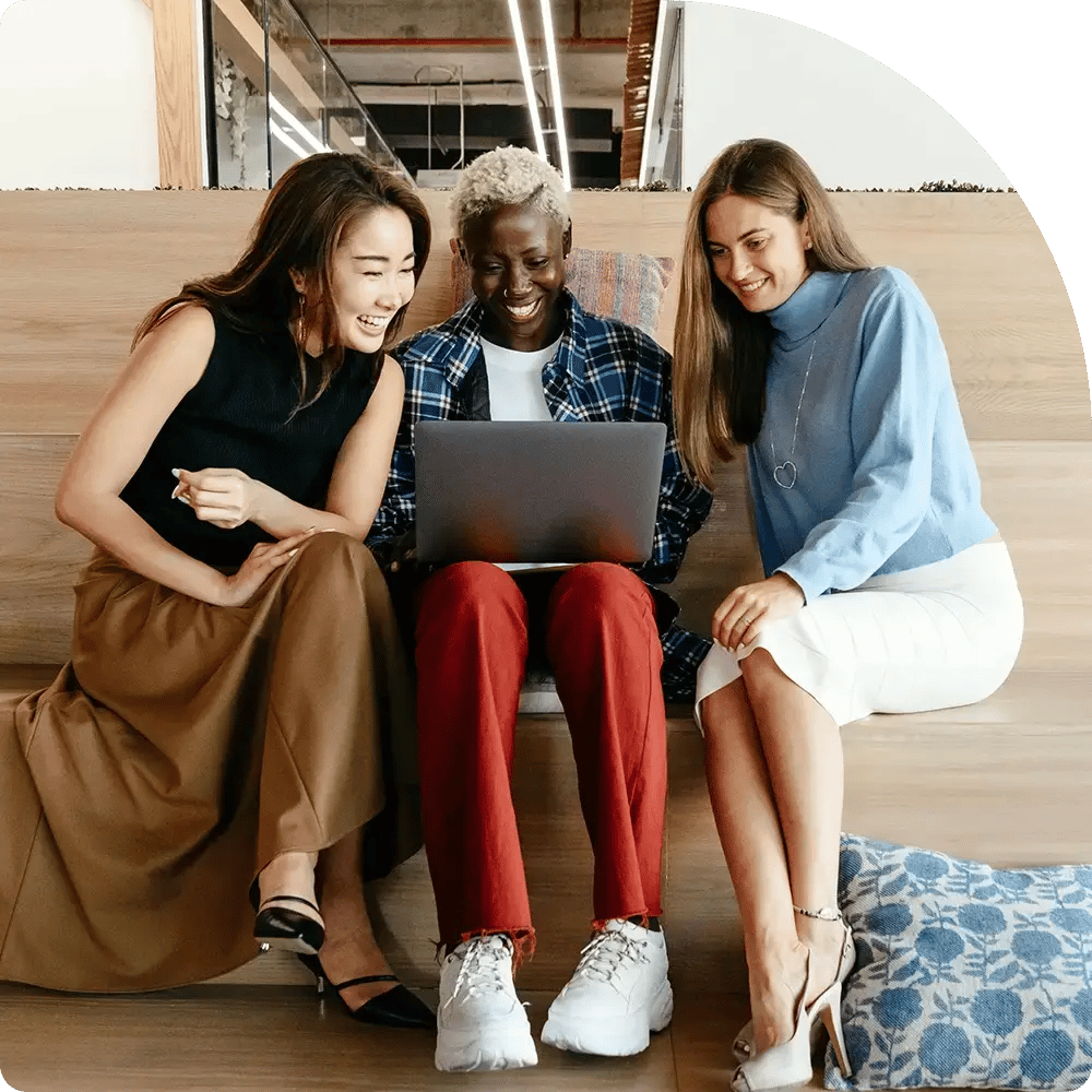 Three smiling young adults gather around a laptop.