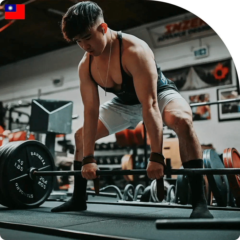 A person is performing a deadlift in a gym, wearing a tank top and shorts, with an intense focus. The gym is filled with weights and equipment.