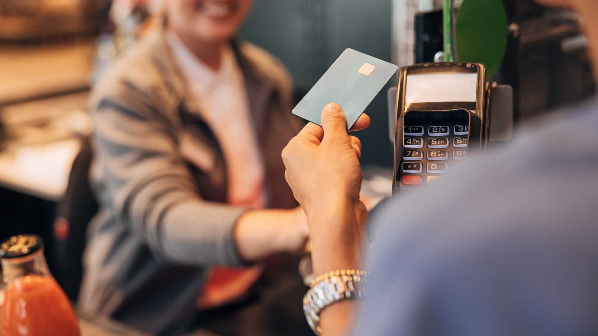 A person making a contactless payment using a credit card at a POS. The cashier is smiling. 