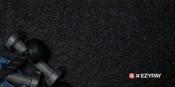 The Gymdesk logo appears next to the Ezypay logo on a black gym mat. 