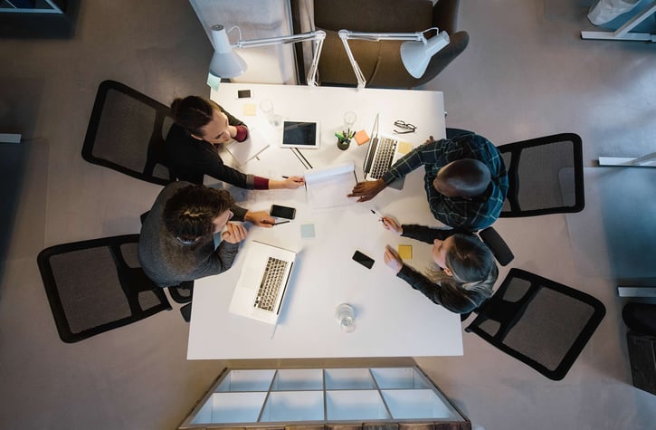 Top-down view of a diverse business team collaborating around a white conference table with laptops and documents.