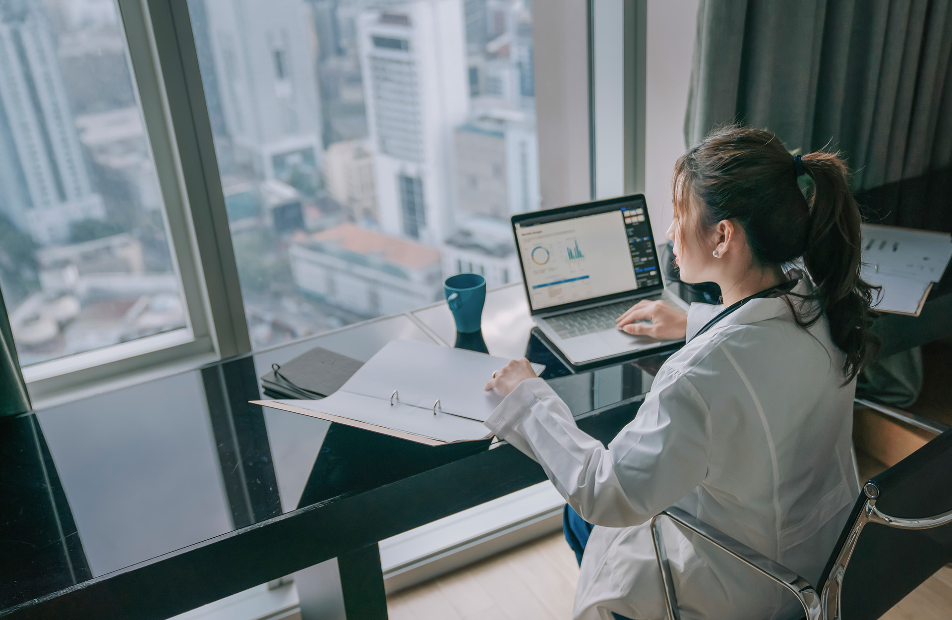 Professional reviewing business performance data and analytics dashboard on a laptop in a modern office overlooking a city skyline.
