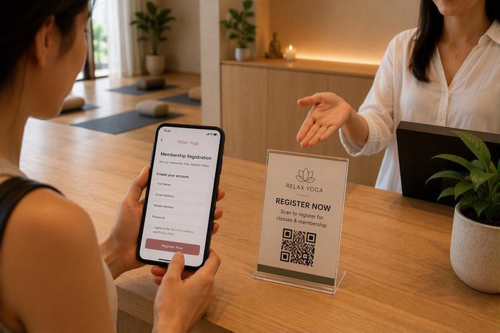 A new member registering for a Relax Yoga membership using a smartphone and QR code registration stand at the studio reception counter.
