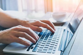 Two hands hover over a laptop keyboard