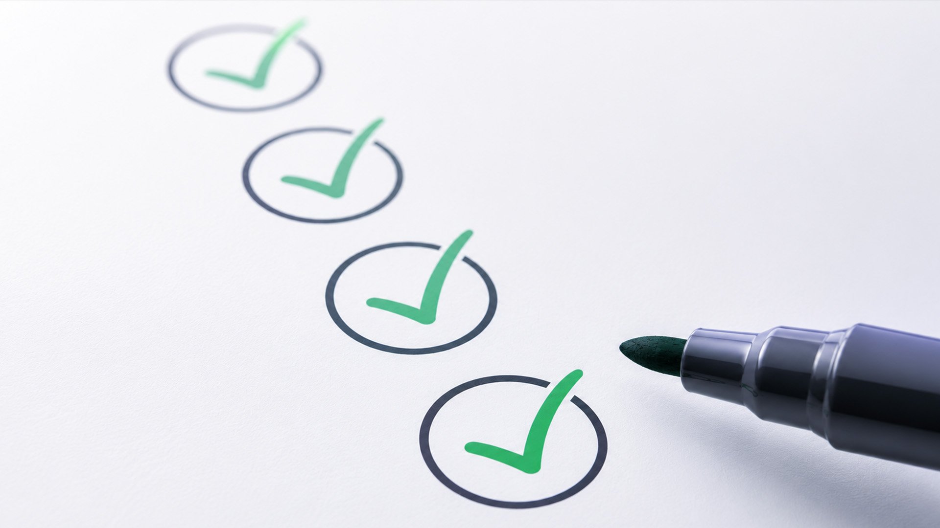 A row of four green checkmarks inside black circles on white paper, with a green marker beside them. The image conveys a sense of completion.