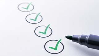 A row of four green checkmarks inside black circles on white paper, with a green marker beside them. The image conveys a sense of completion.