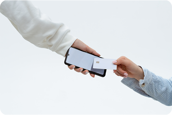 Two hands exchanging items: one holds a smartphone, the other a white credit card.