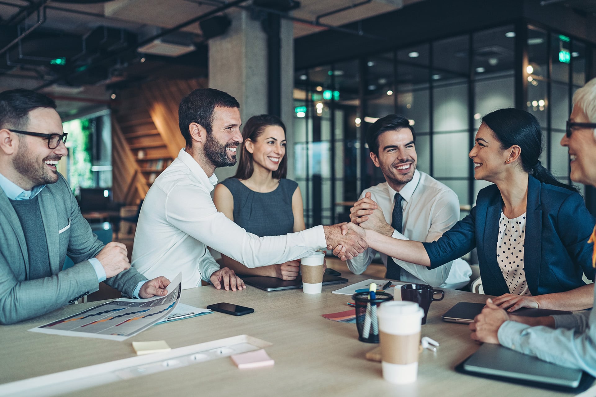 Business professionals shaking hands during a partnership meeting in a modern office boardroom, discussing collaboration and business growth.