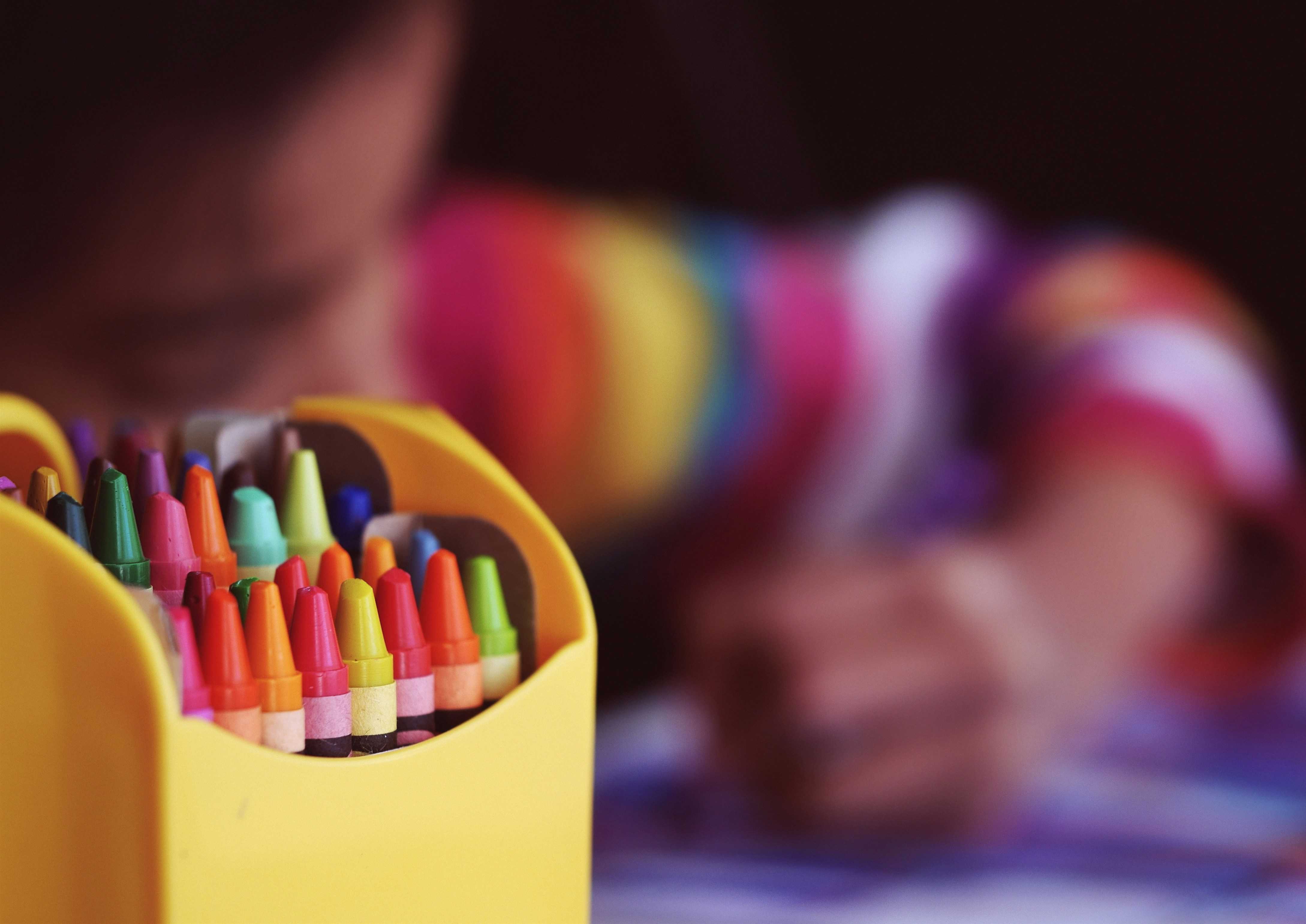 A child drawing with some colourful crayons. They are stored inside a yellow box.