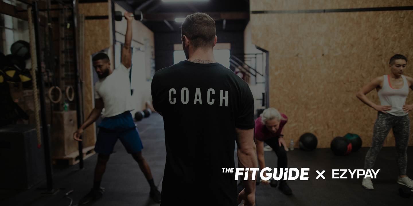 The image captures a dynamic scene inside a modern gym or fitness studio, where a coach is centrally positioned with their back facing the viewer. The word