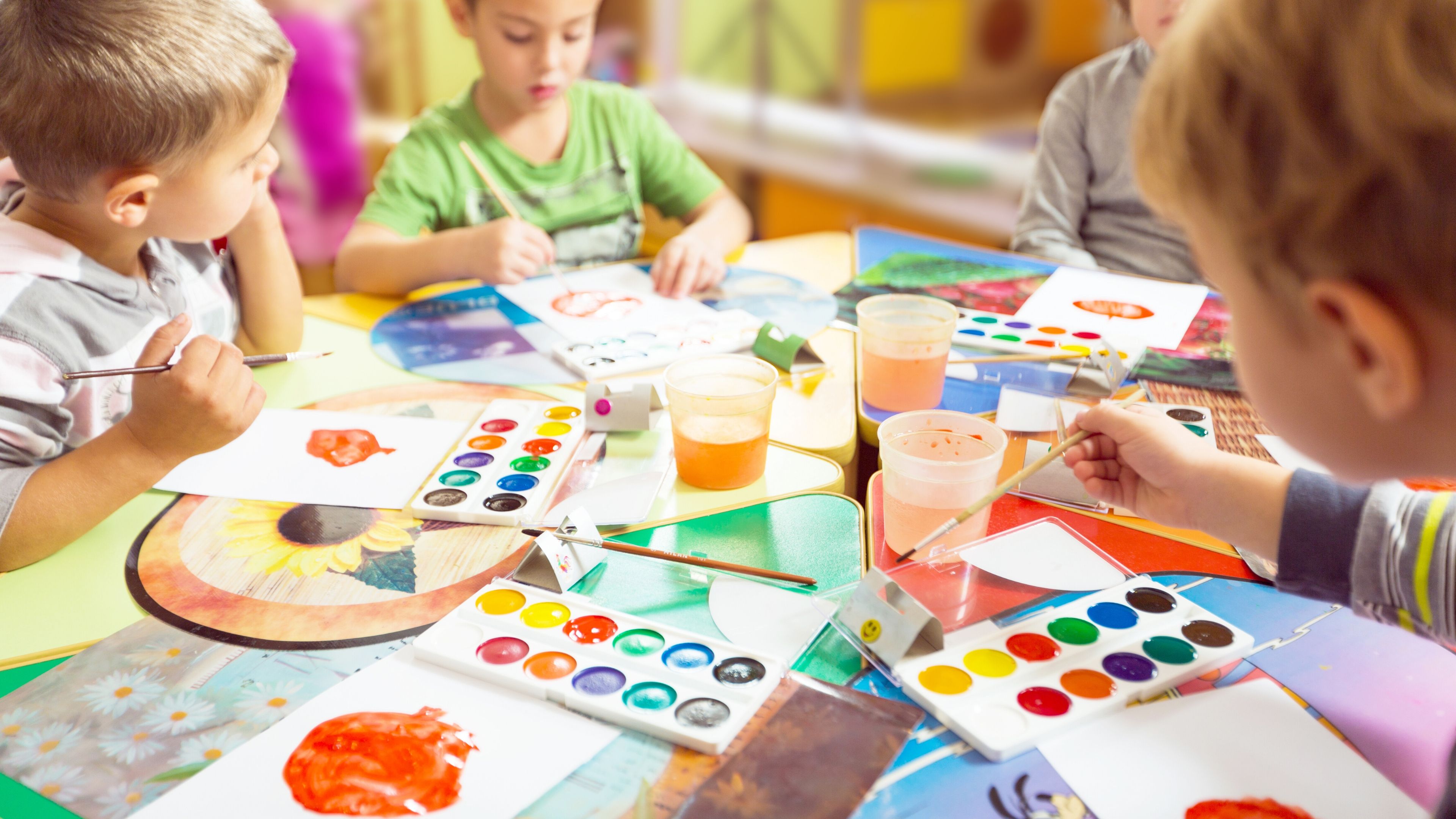 Children sitting around a table. They are painting with brightly coloured paints. 
