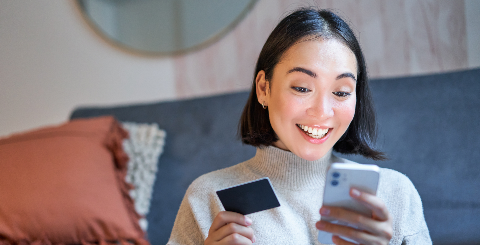 A smiling woman holds a credit card and her smartphone. 